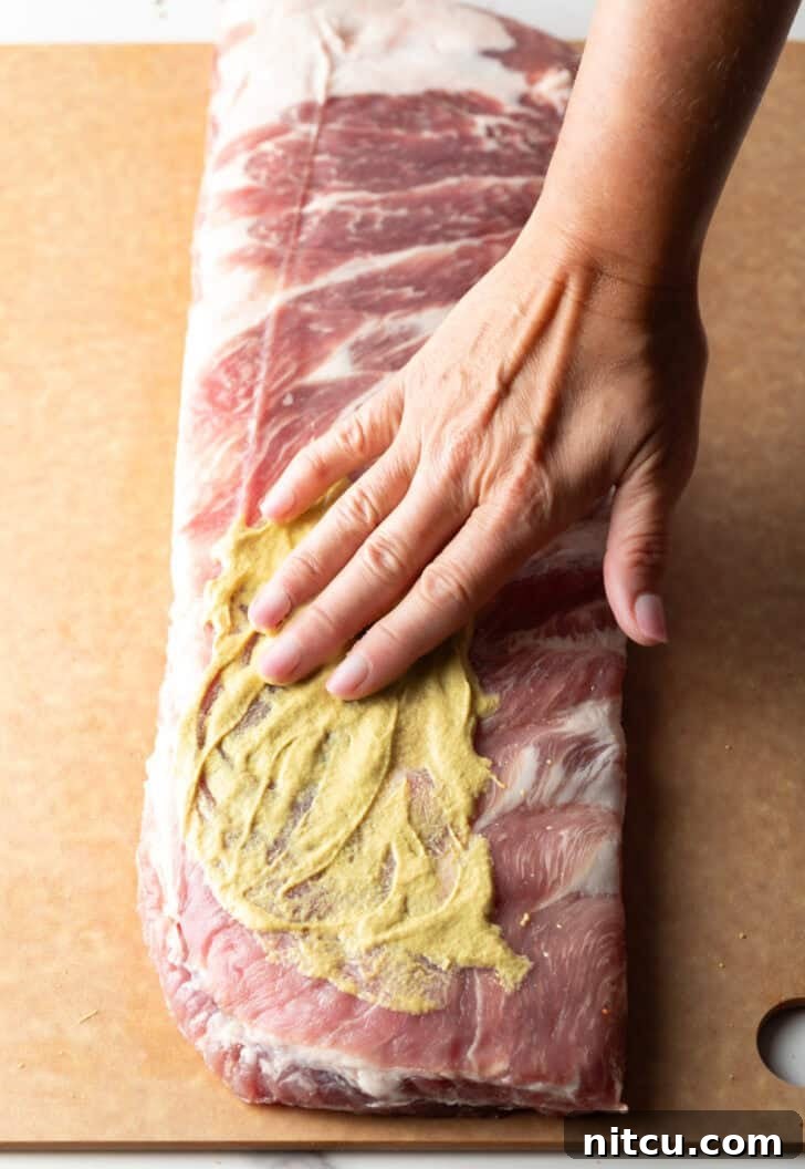Gateway City Ribs 7 Overhead shot of a raw rack of St. Louis pork ribs being generously smeared with Dijon mustard.
