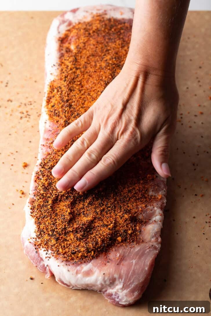 Gateway City Ribs 8 Overhead shot of a raw rack of pork ribs with a hand applying dry rub seasoning.