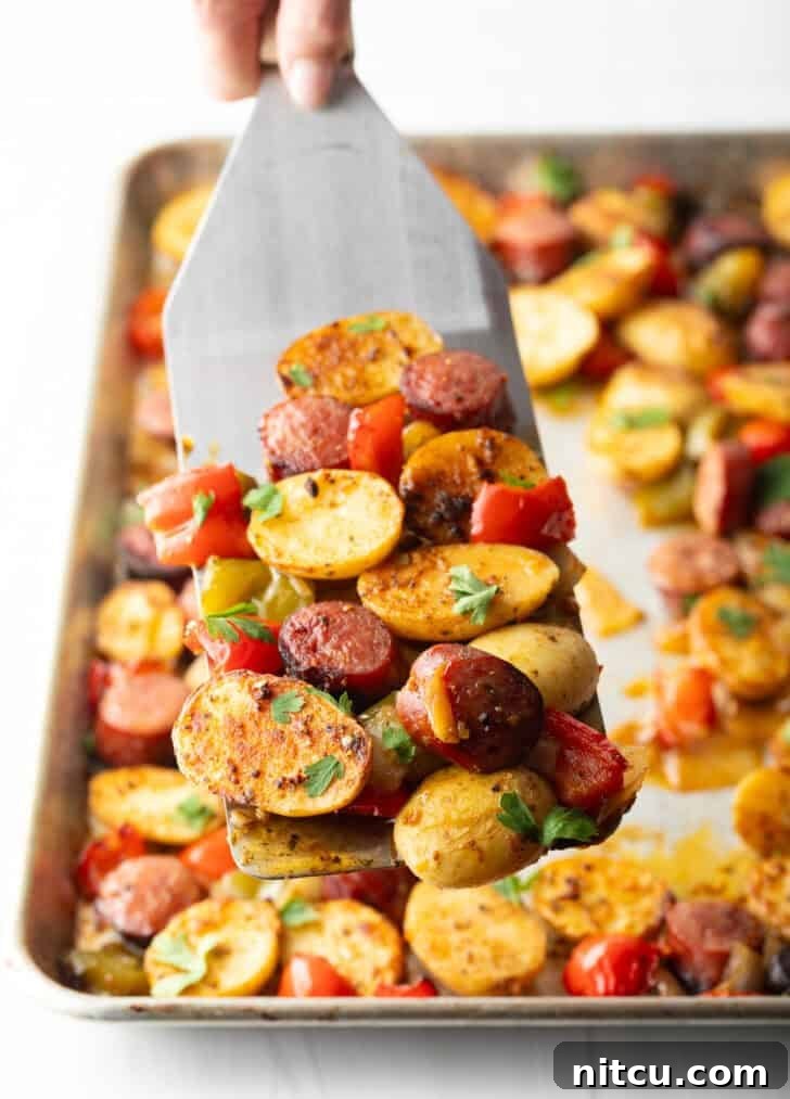 Smoky Sausage and Roasted Potatoes 9 Metal spatula holding up a scoop of roasted kielbasa, potatoes, and red peppers from the sheet pan.