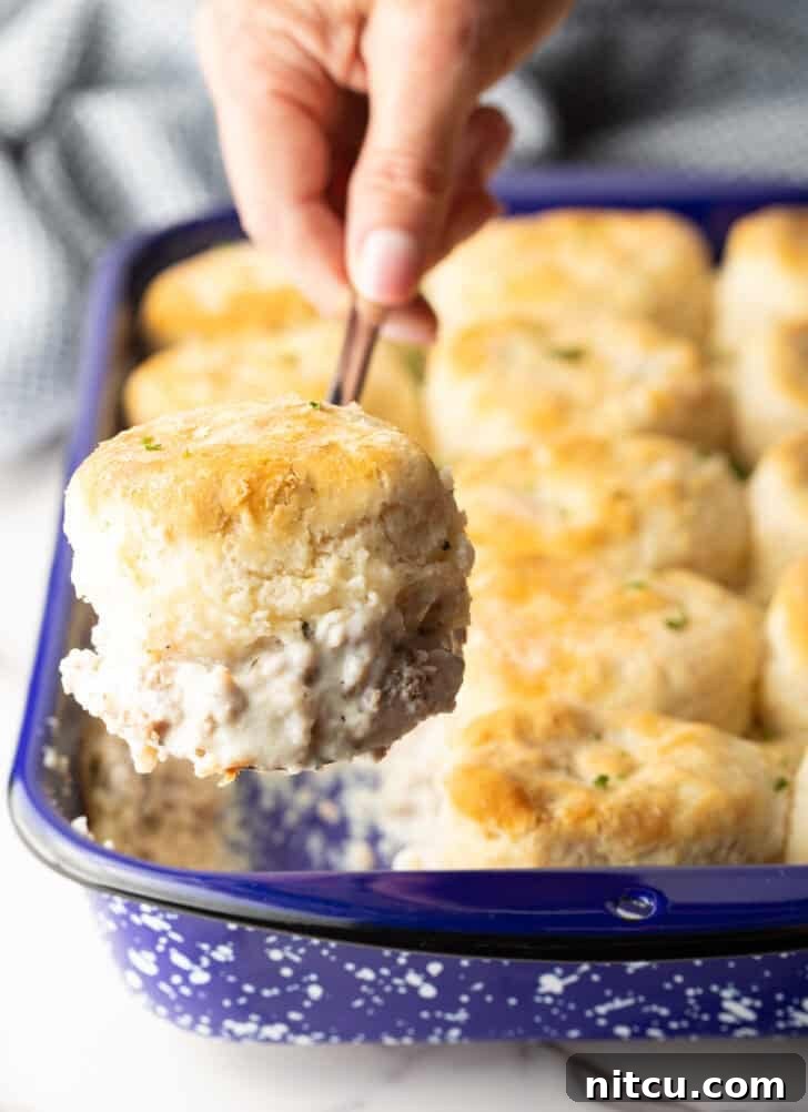 Golden brown Biscuits and Gravy Casserole lifted out of a baking pan, showing the layers of fluffy biscuits and creamy sausage gravy.