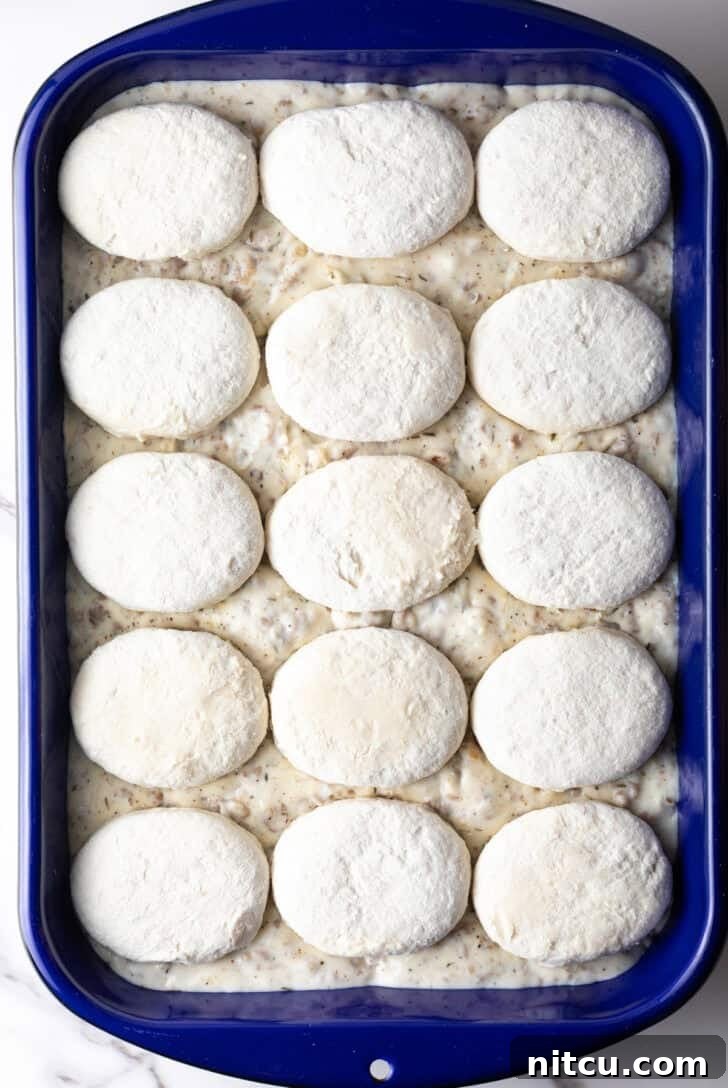 Frozen biscuits lined up on top of a blue pan filled with sausage gravy.