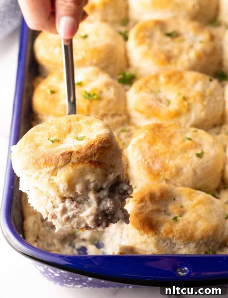 A metal spatula taking a scoop of biscuits and gravy breakfast casserole from the pan, showing the golden biscuit and creamy gravy.