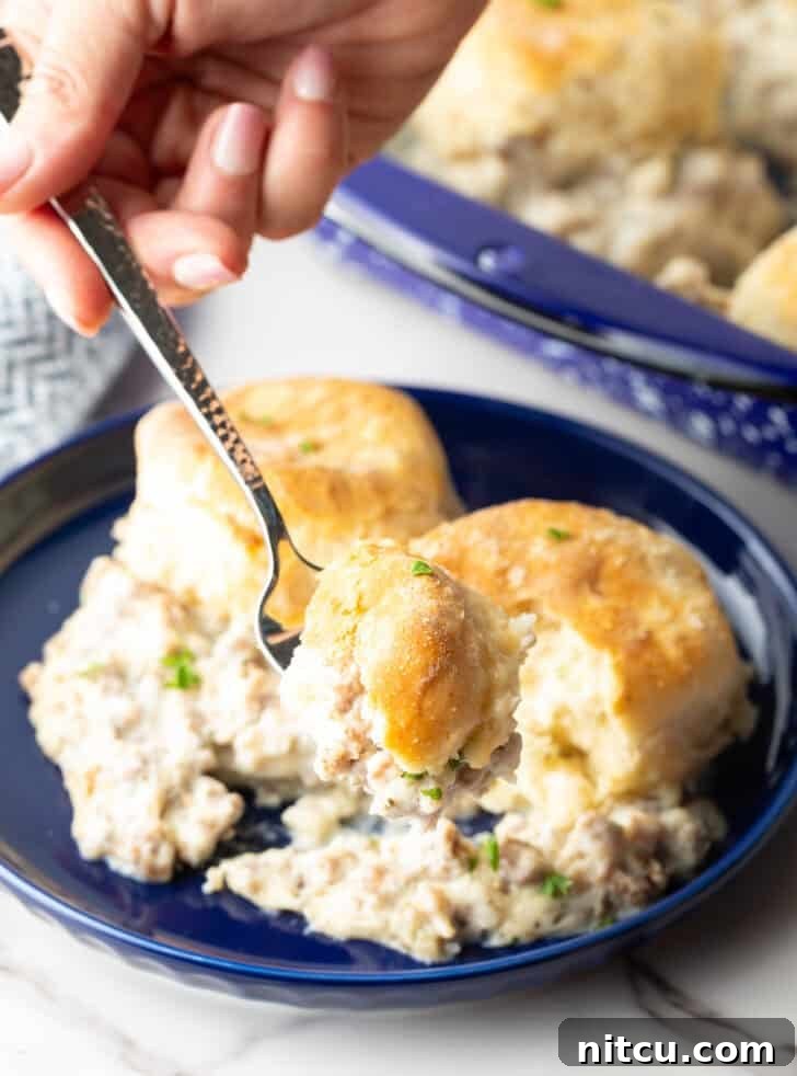 A blue plate with a serving of sausage biscuits and gravy casserole, with a fork holding a bite.
