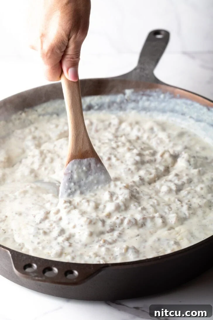 Sausage gravy being stirred with a wooden spoon in a pan.