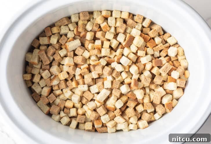 Effortless Crock Pot Stuffing 6 Dried bread cubes in a white crock pot.