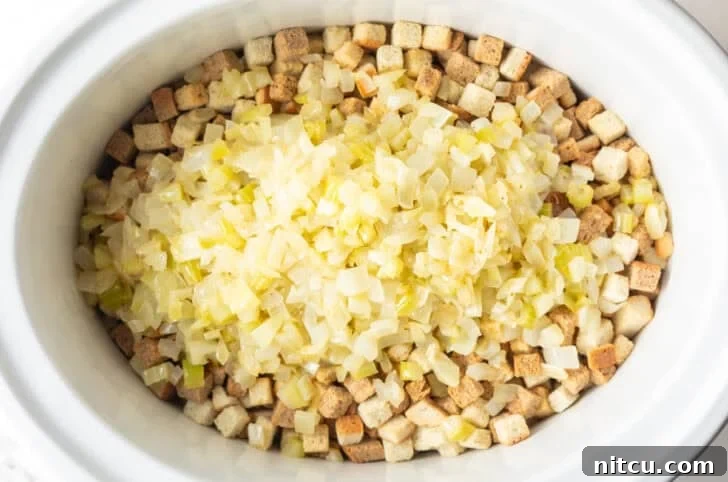 Effortless Crock Pot Stuffing 7 Dried bread cubes topped with cooked onions in a white crock pot.