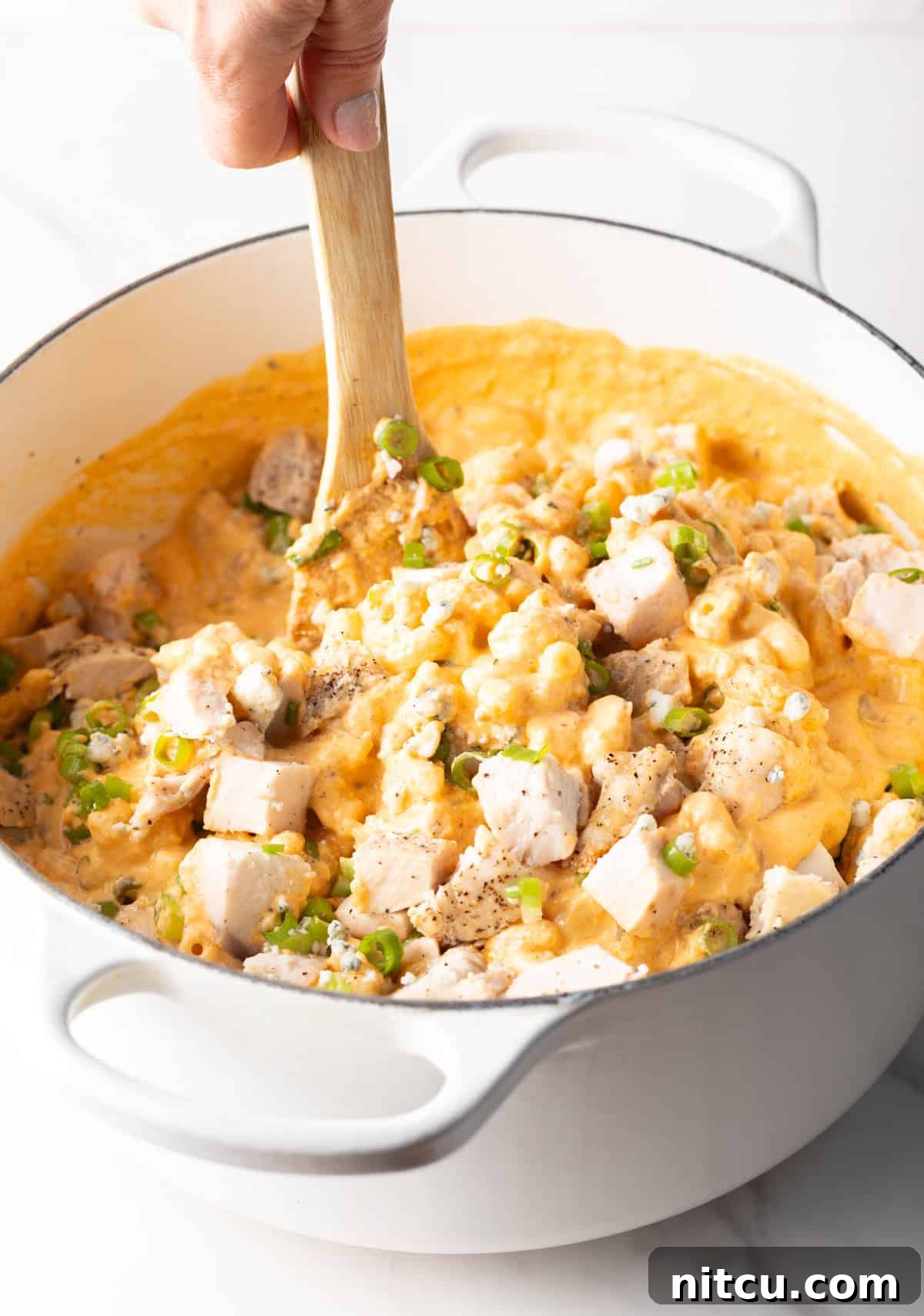 Using a wood spoon to stir cooked chopped chicken in a pot of macaroni and cheese.
