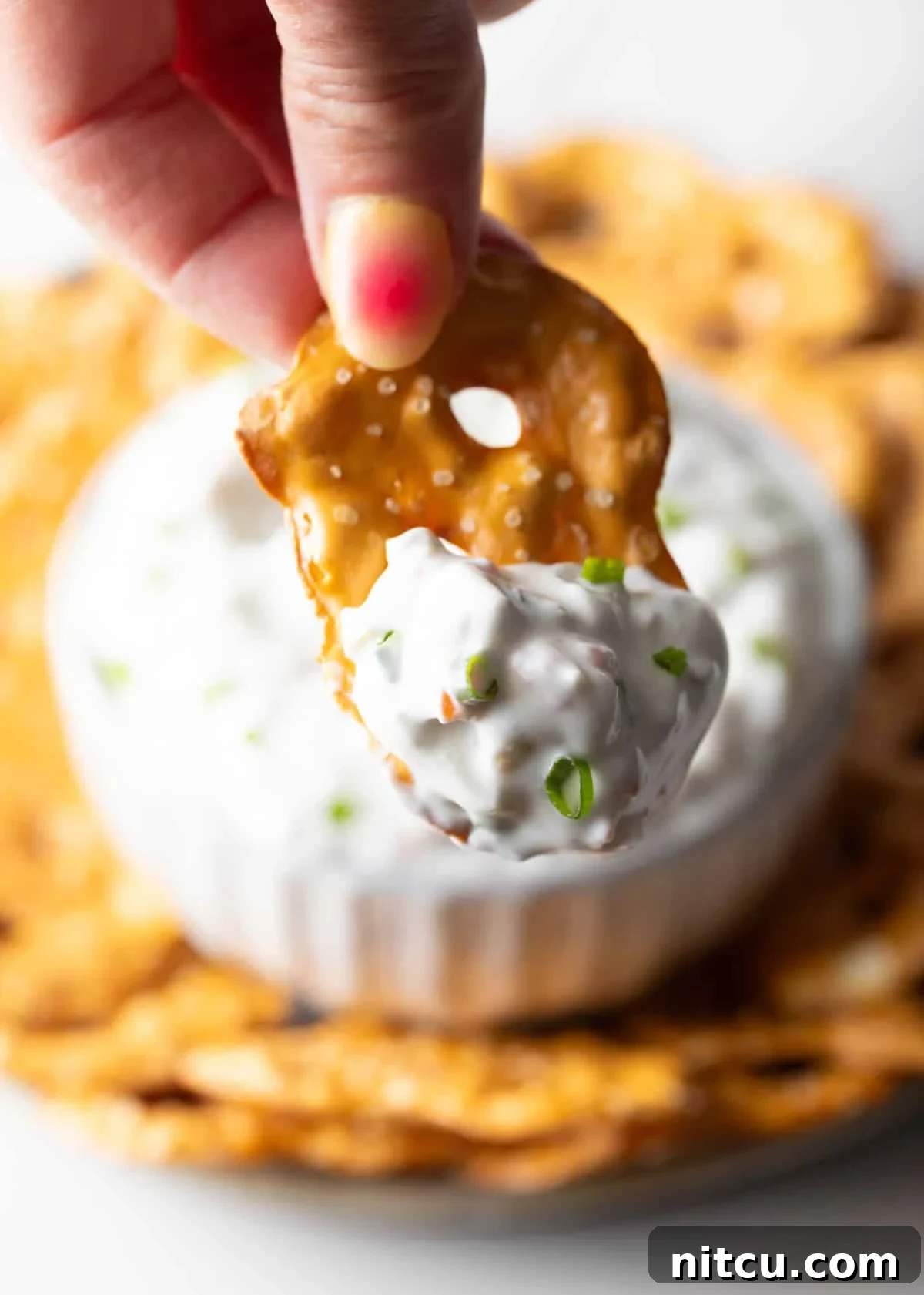 Hand holding a pretzel chip generously scooped with olive dip, presented towards the camera.