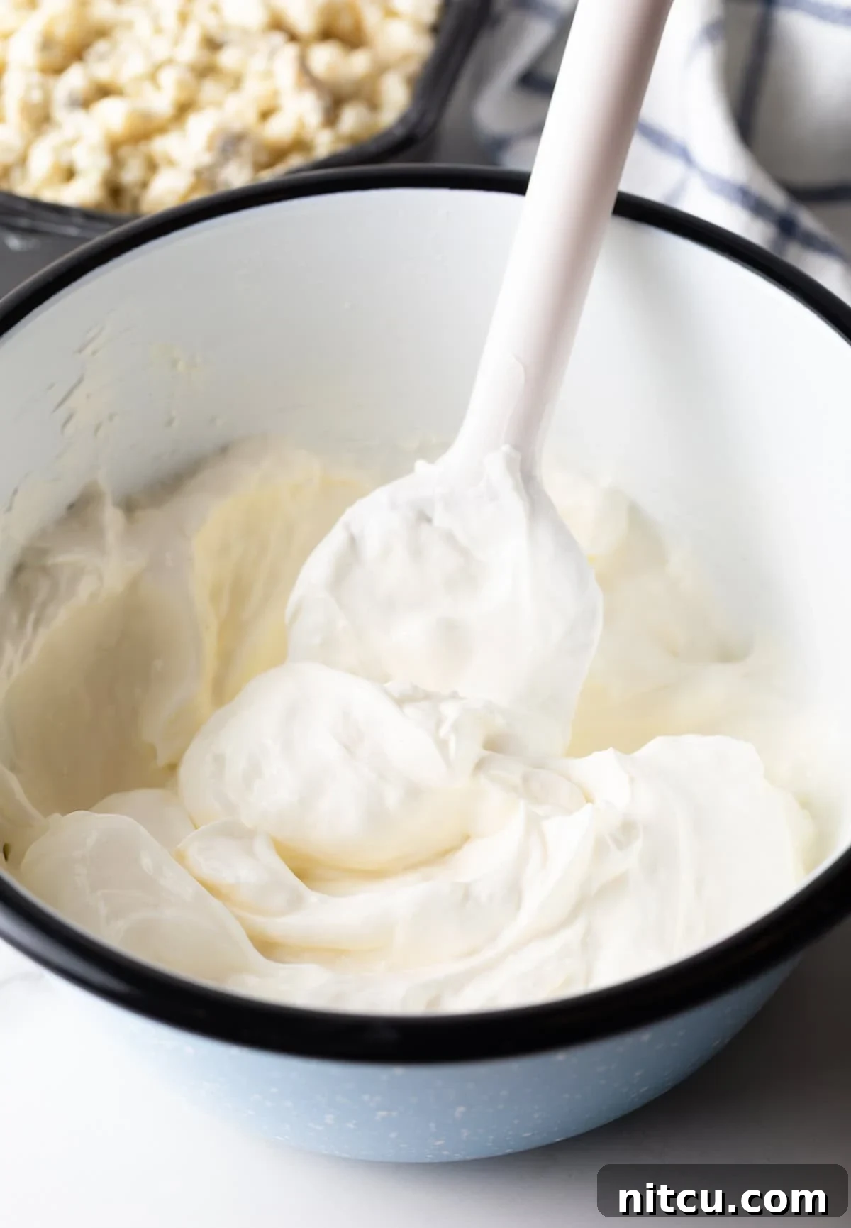 White bowl with cream cheese and sour cream being stirred with a white spatula to a smooth consistency.
