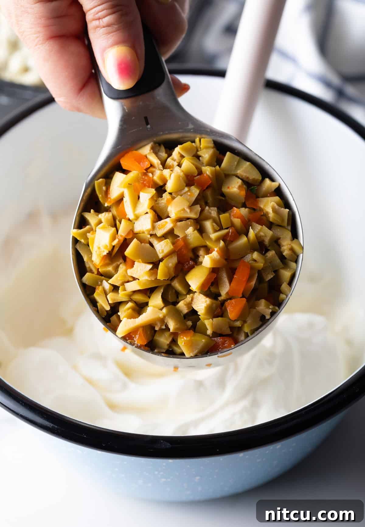 A measuring cup filled with finely chopped green olives, ready to be added to the dip.