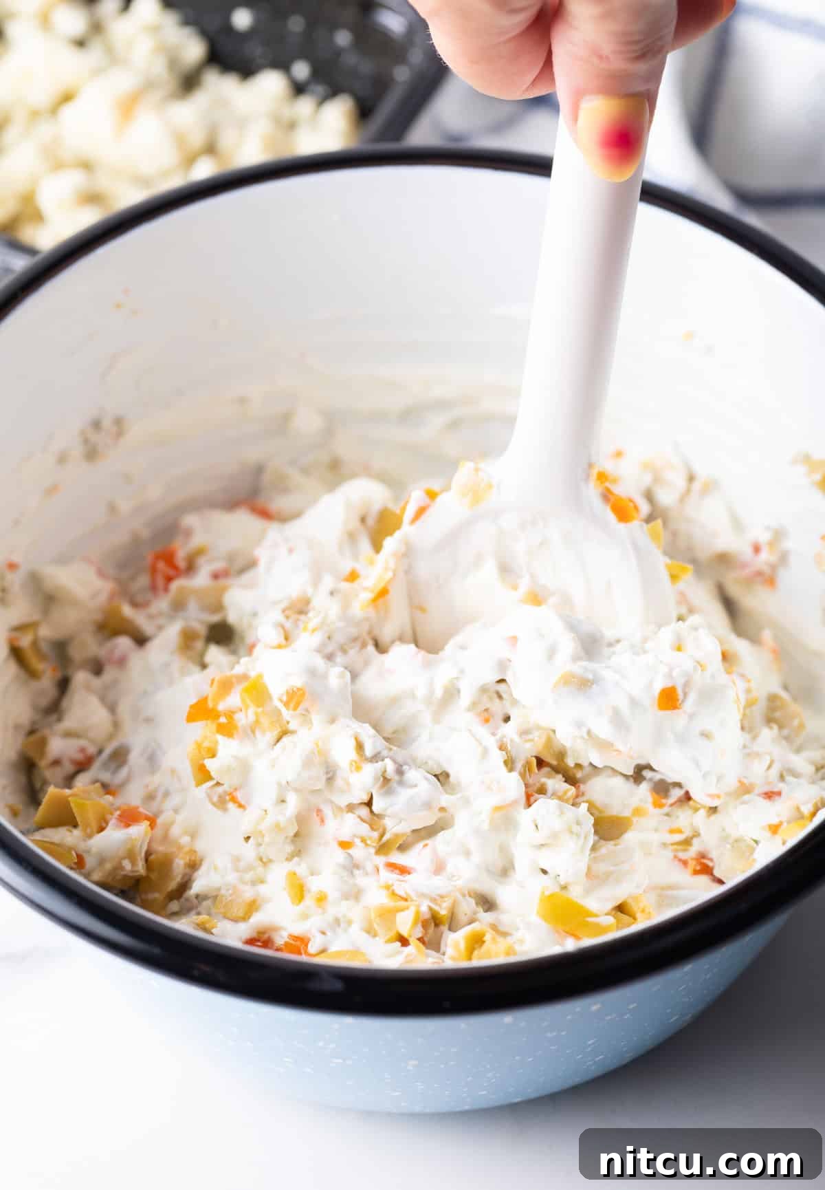 Stirring all the dirty martini dip ingredients together in a white bowl with a white spatula until fully combined.