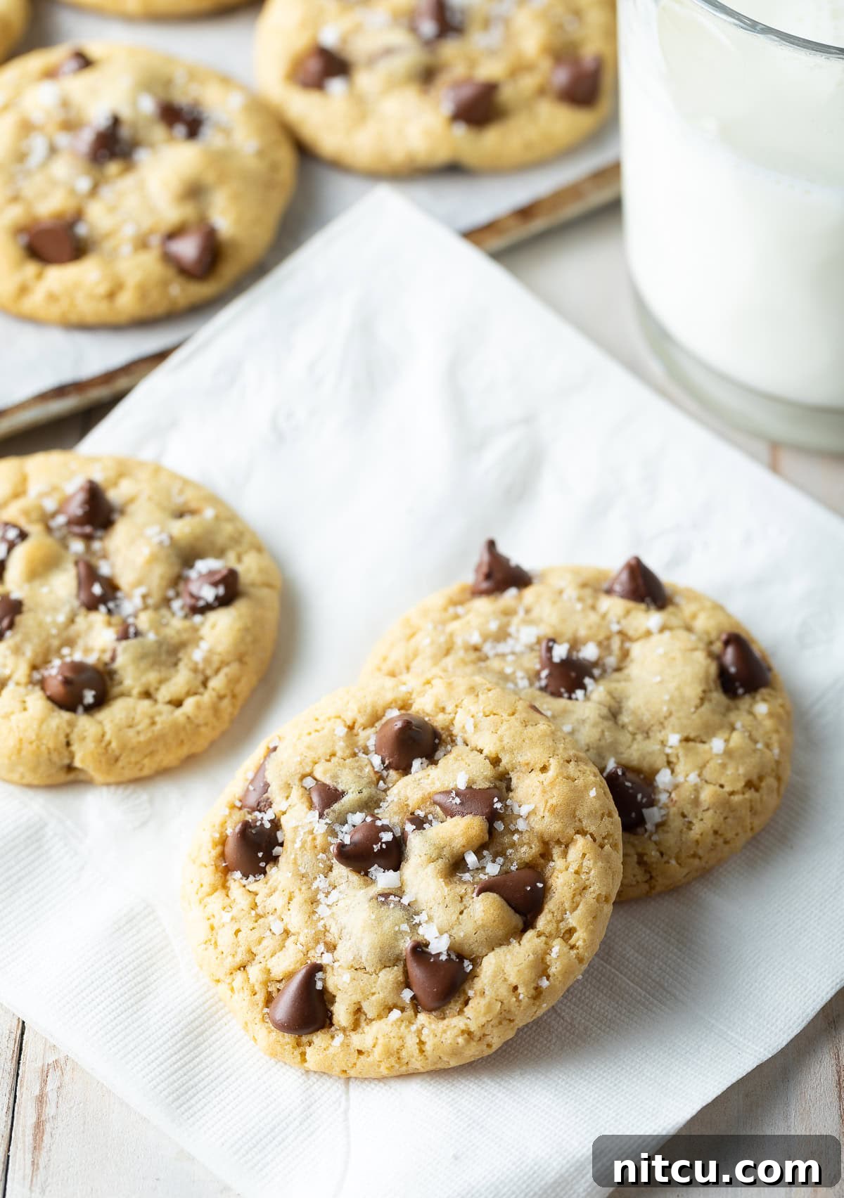 Salted Chocolate Chip Cookie Bliss 5 Three perfectly baked salted chocolate chip cookies arranged on a pristine white napkin, showcasing their golden edges and melted chocolate.