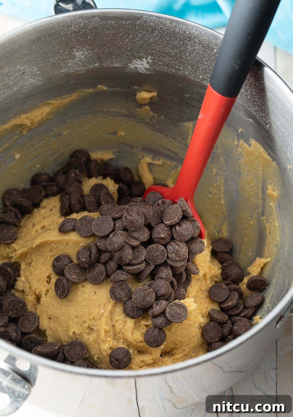 Salted Chocolate Chip Cookie Bliss 8 A red spatula stirring generous amounts of chocolate chips into a bowl of rich, thick cookie dough.
