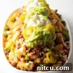 Ultimate Loaded Tots 13 Large white oval serving dish loaded with tater tot nachos with ground beef, jalapenos, salsa, cheddar cheese, guacamole and sour cream.