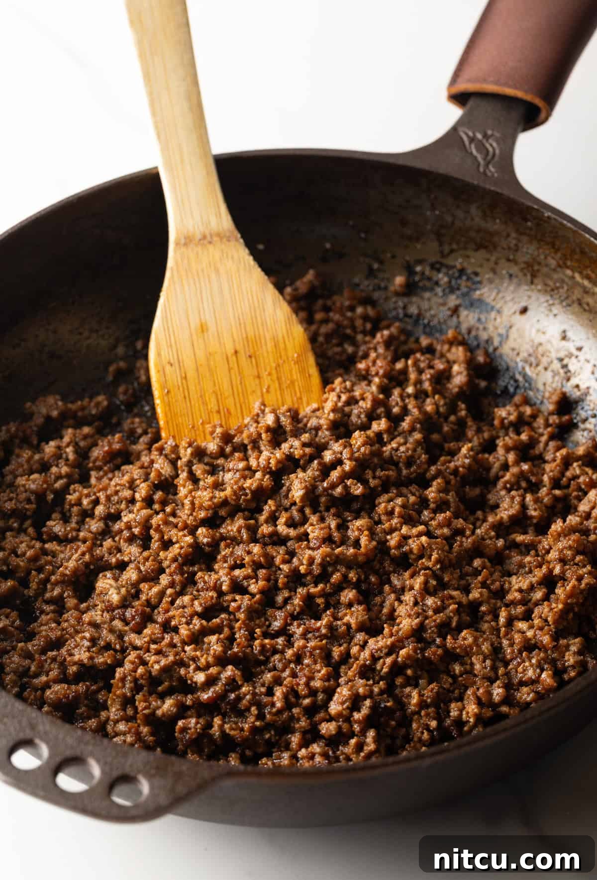 Ultimate Loaded Tots 7 Cooking crumbled ground beef in a large skillet with a wooden spatula.