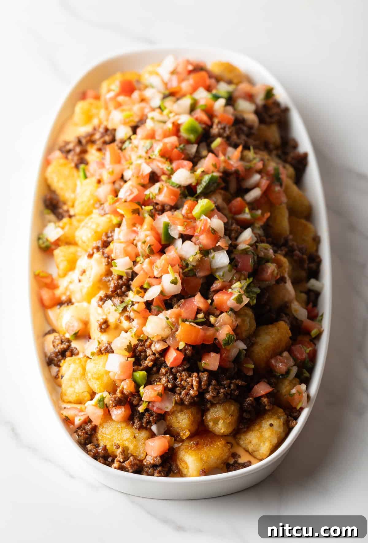 Ultimate Loaded Tots 10 Tater tots in a large white oval bowl covered with ground beef and pico de gallo.