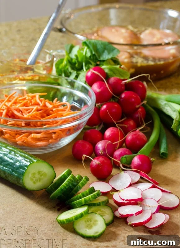 Deconstructed Banh Mi Salad 3 Recipe ingredients beautifully displayed: Whole and thinly sliced radishes, fresh sliced cucumber, vibrant whole green onions, and a glass bowl overflowing with finely shredded carrots. These are key components for a refreshing Banh Mi salad.