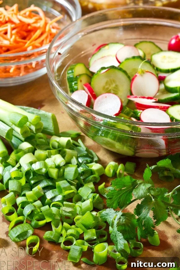 Deconstructed Banh Mi Salad 4 Close-up of freshly prepped ingredients for a Banh Mi salad: A neat pile of thinly sliced green onions and a clear glass bowl filled with perfectly sliced cucumbers and radishes soaking in a light pickling liquid. Ready for assembly!