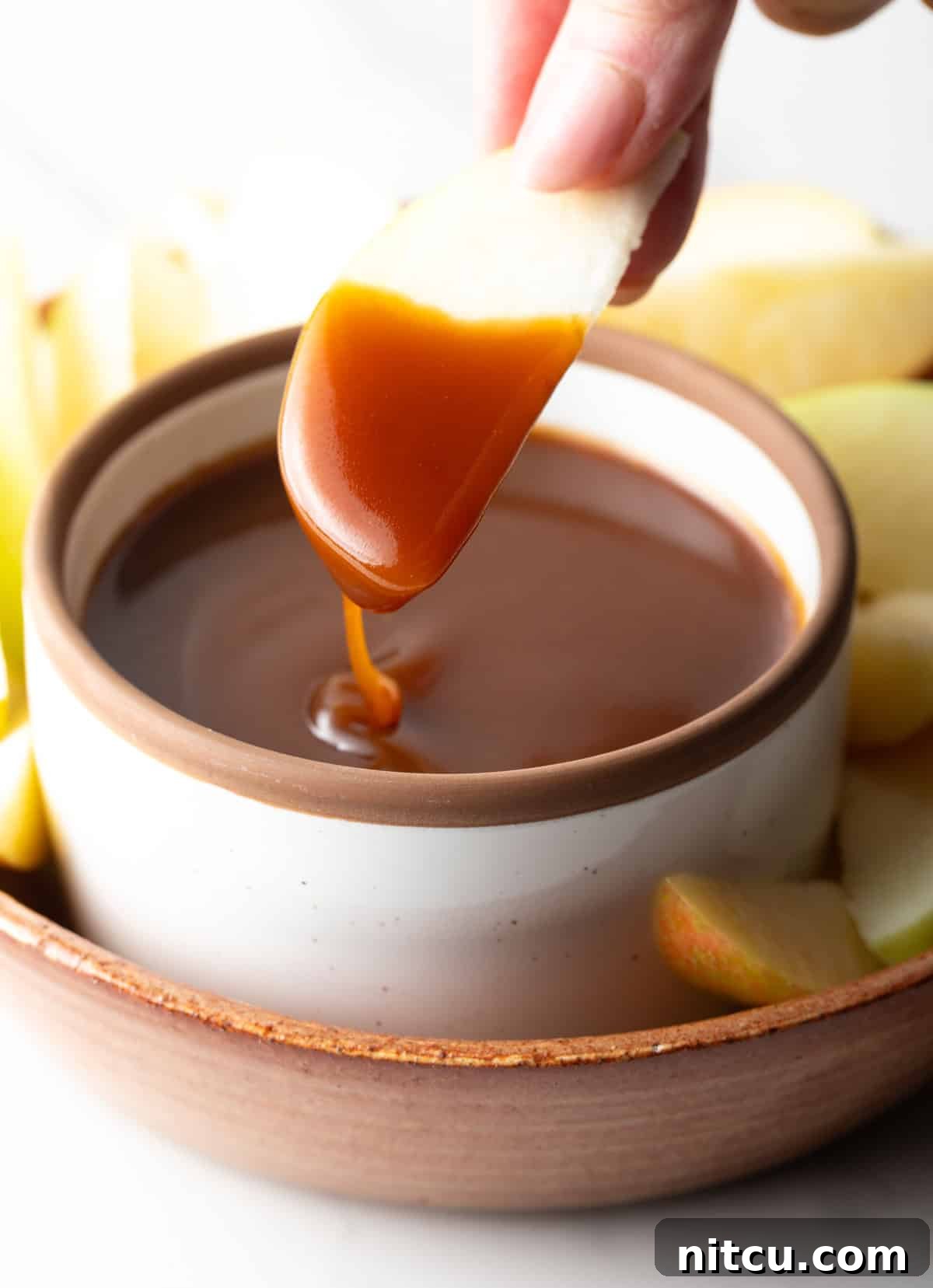 Salted Caramel Delight 11 An apple slice being dipped into a container of salted caramel sauce.