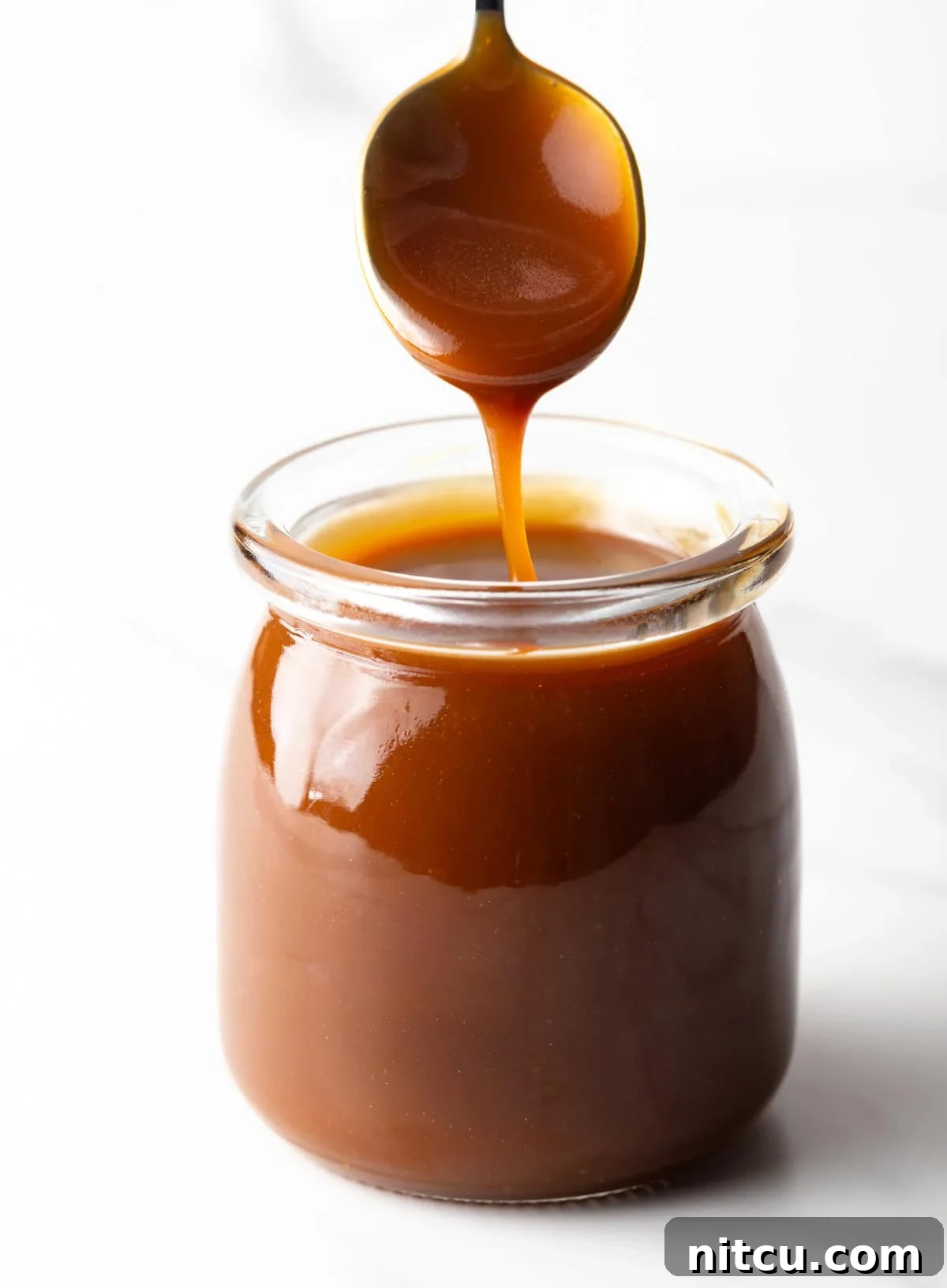 Salted Caramel Delight 3 Homemade salted caramel sauce being drizzled with a spoon into a glass jar.