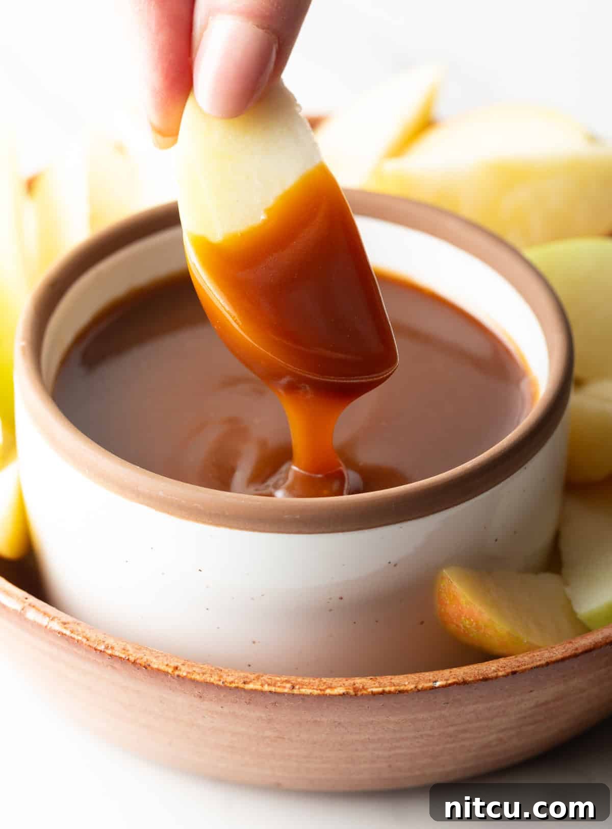 Salted Caramel Delight 5 An apple sliced that's been dipped into salted caramel sauce hovering over a jar of sauce.