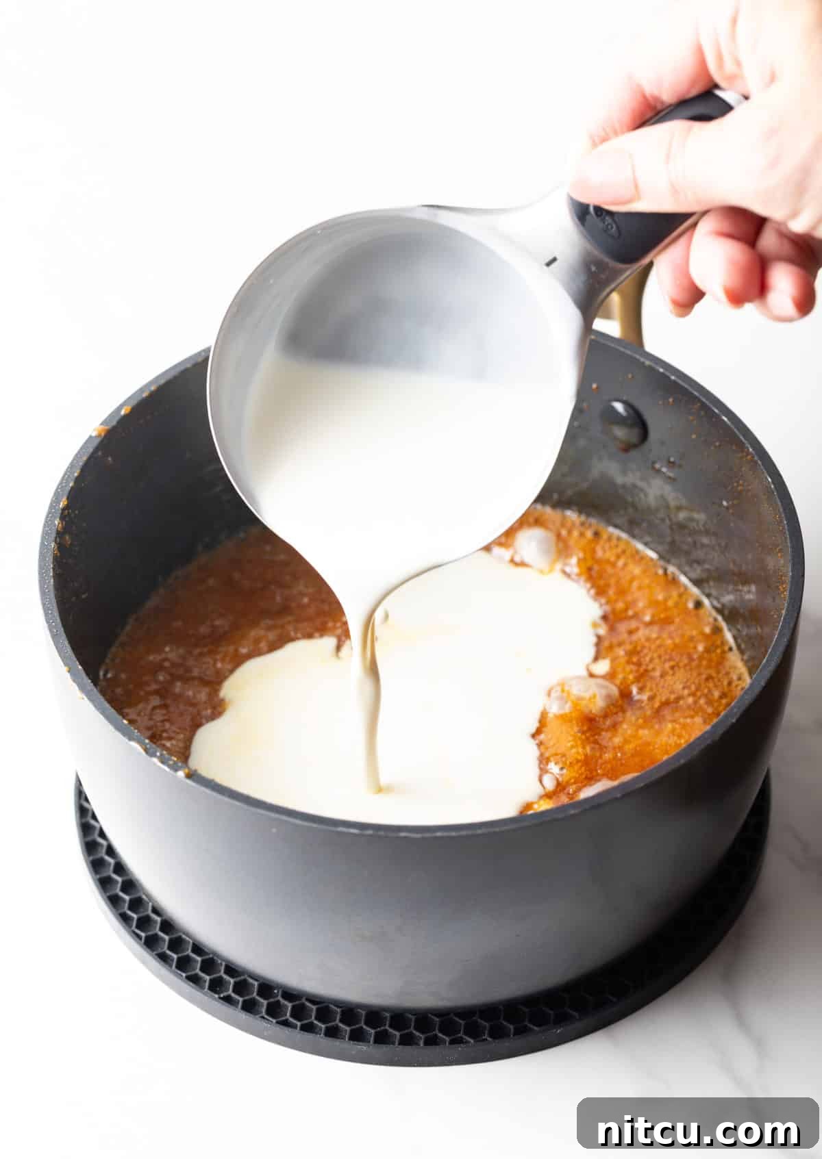 Salted Caramel Delight 7 Cream being added to salted caramel sauce mixture in a black sauce pot.