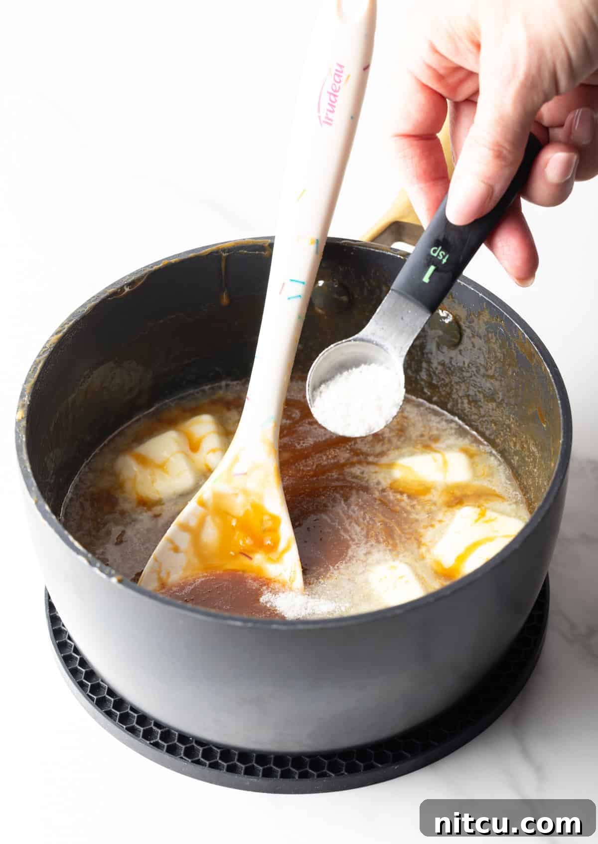 Salted Caramel Delight 8 Ingredients being added to salted caramel sauce in a black sauce pan.