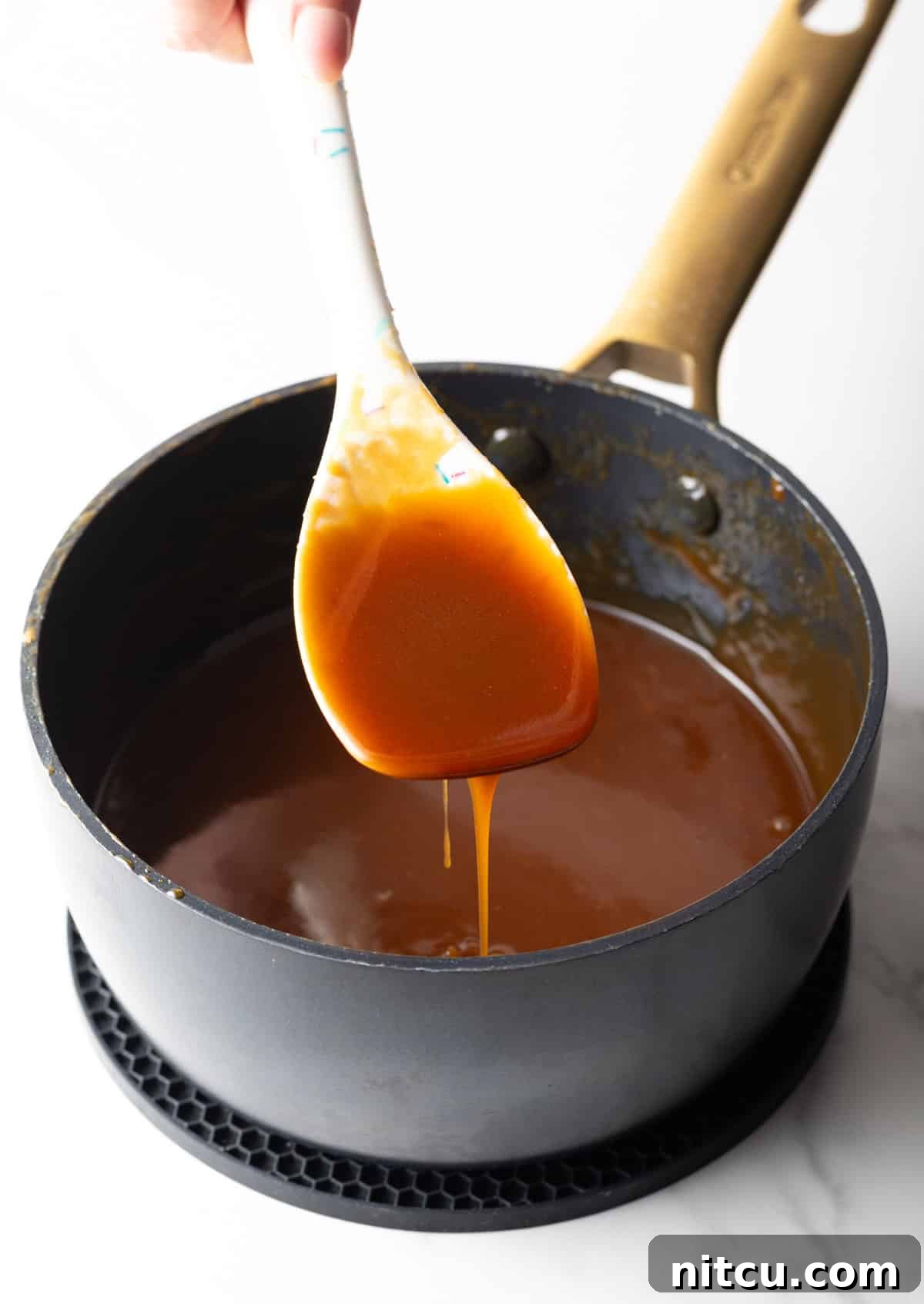 Salted Caramel Delight 9 A white spatula holding salted caramel sauce over a black saucepan.