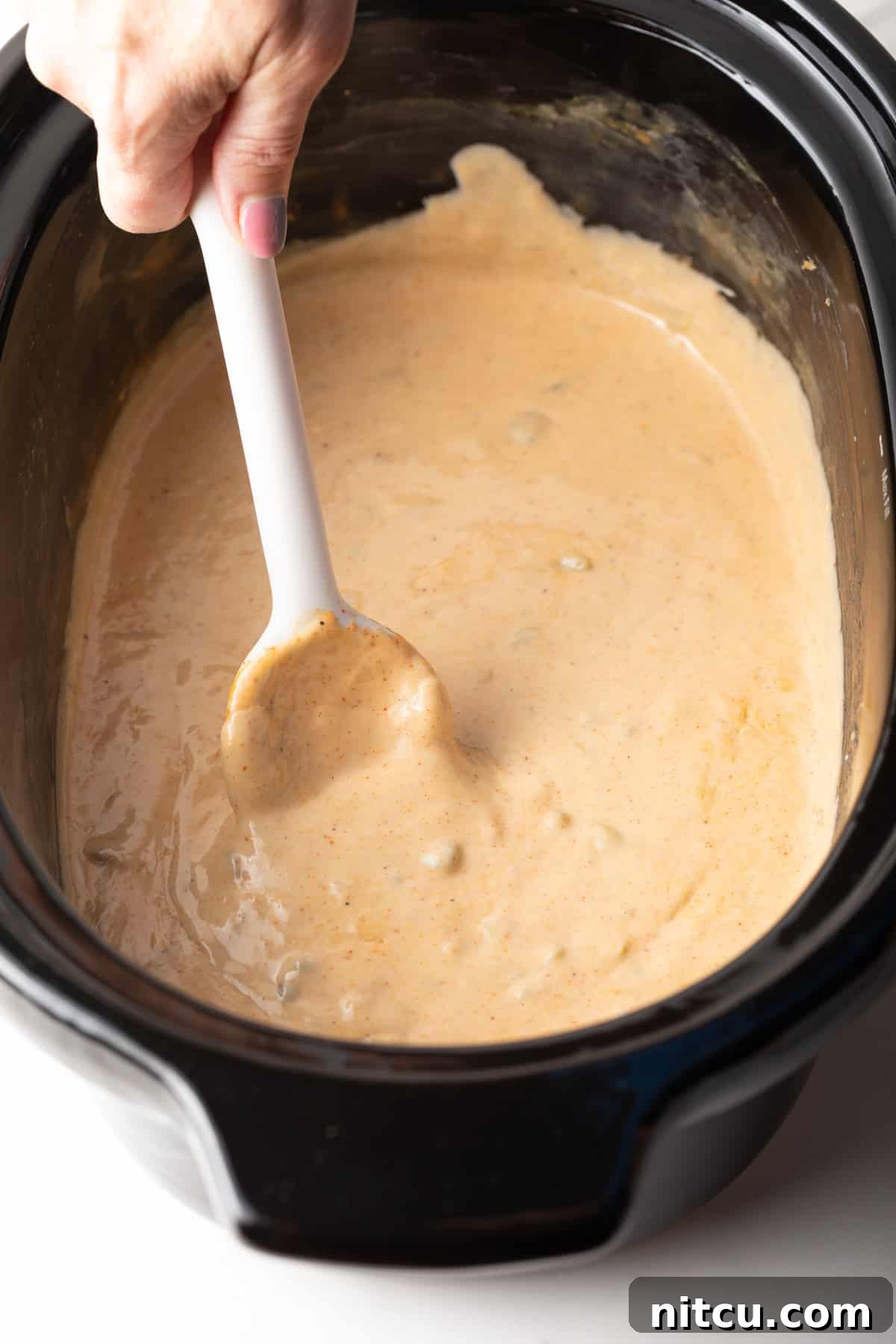 Ultimate Crock Pot Queso Dip 3 A white spoon stirring slow cooker queso dip in a black crock pot.