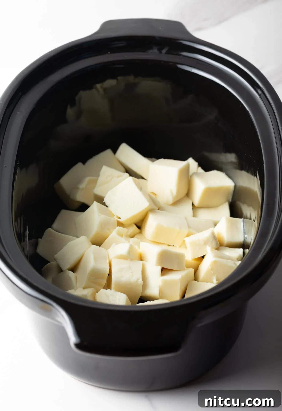 Ultimate Crock Pot Queso Dip 6 Cubed white American cheese sitting in a black crock pot.