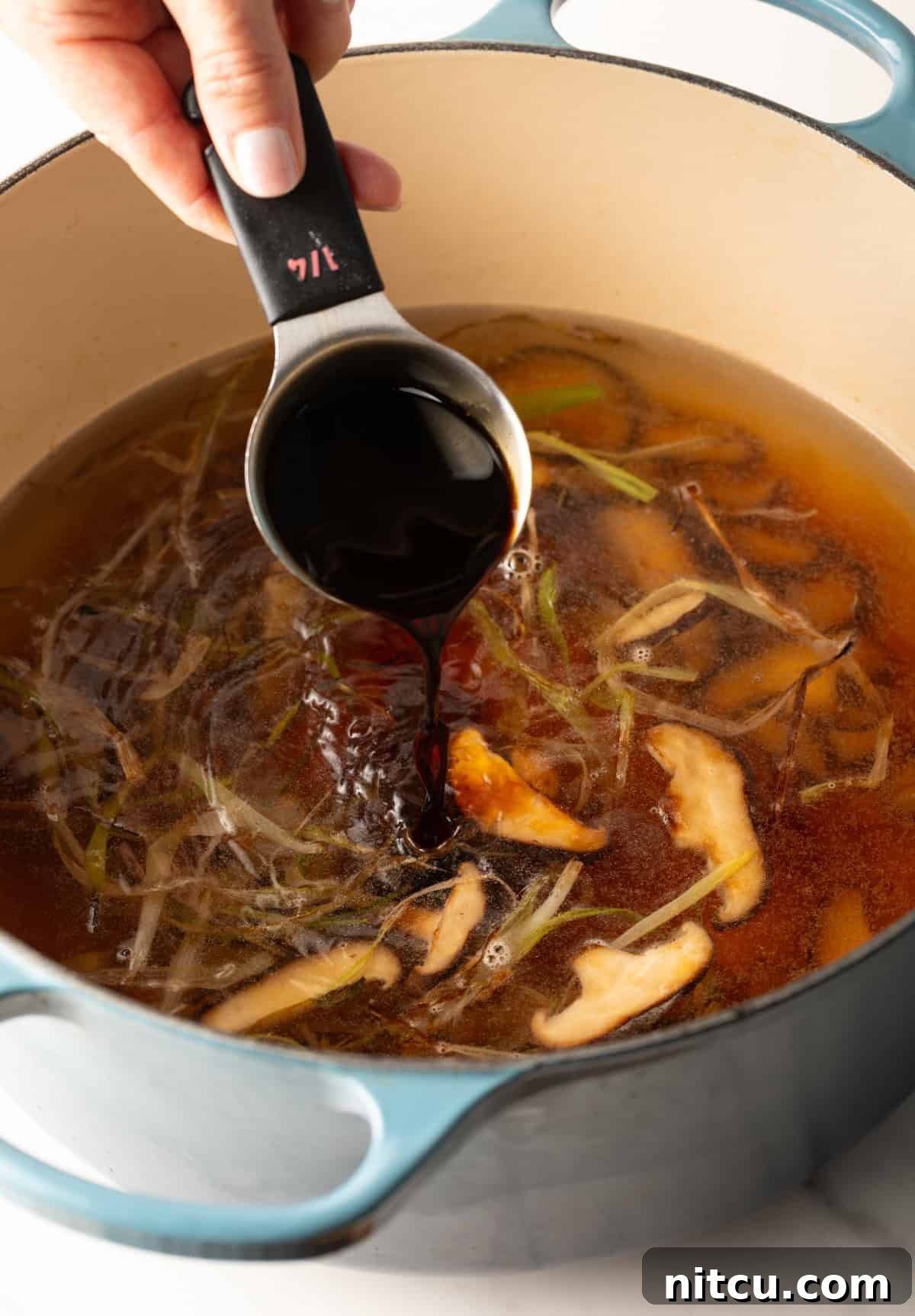 Effortless Udon Bowl 8 A measuring cup adding soy sauce to udon noodle soup broth.