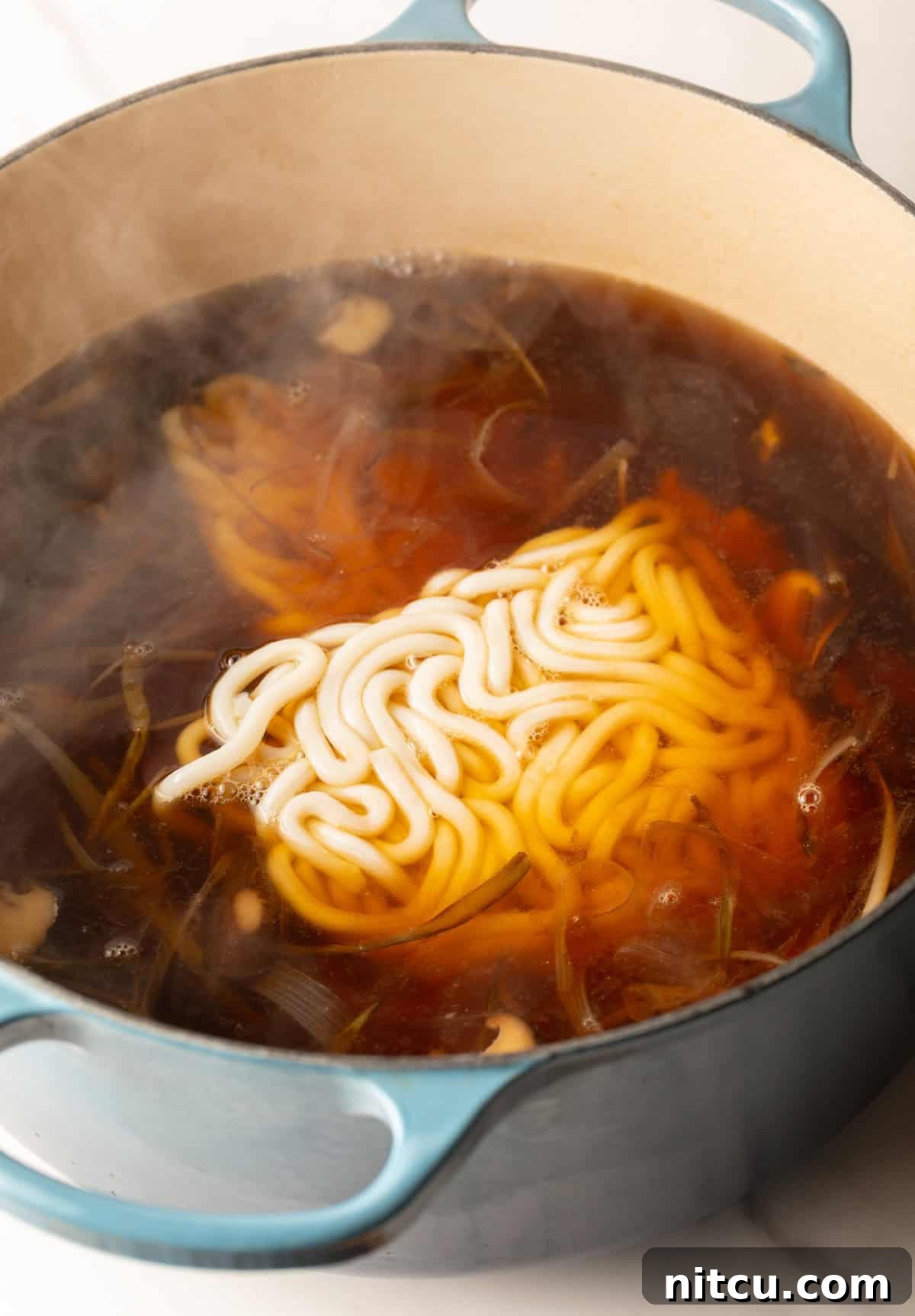 Effortless Udon Bowl 9 Udon noodles being added to the udon noodle soup broth in a pot.