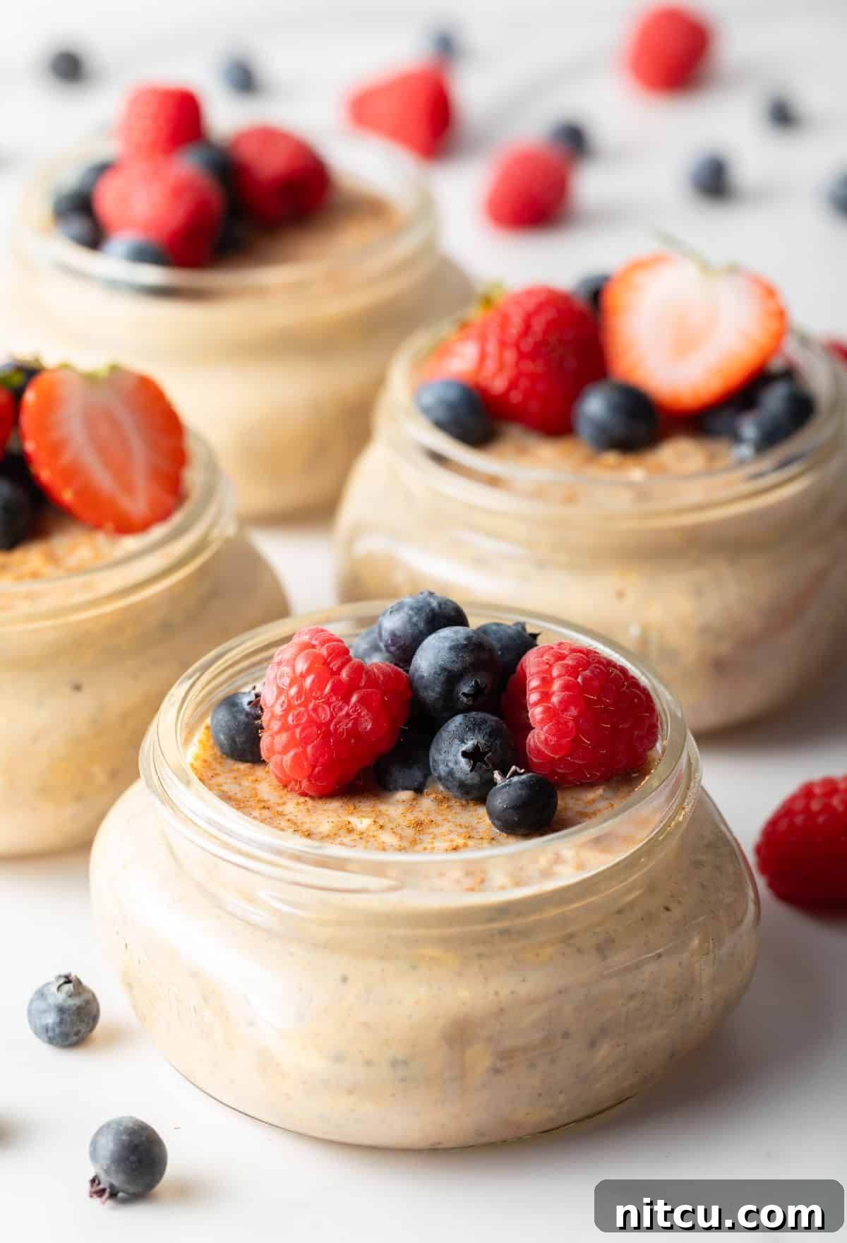 Protein Packed Next-Day Oats 3 Small jars filled with high protein overnight oats topped with raspberries and blueberries.