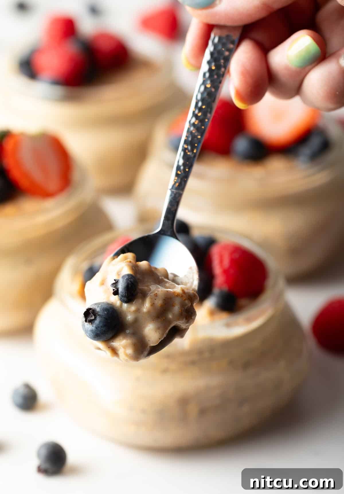 Protein Packed Next-Day Oats 10 A spoon holding a bite of high protein oatmeal above a glass jar.