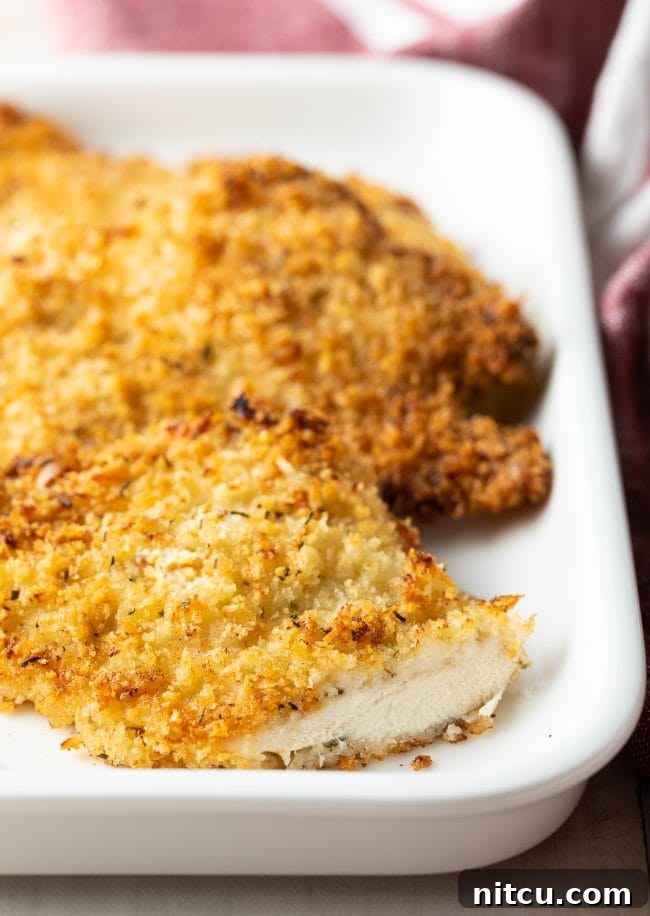 Golden Baked Chicken Cutlets 11 Baked chicken cutlet on a white platter with a slice removed, showing its juicy interior.