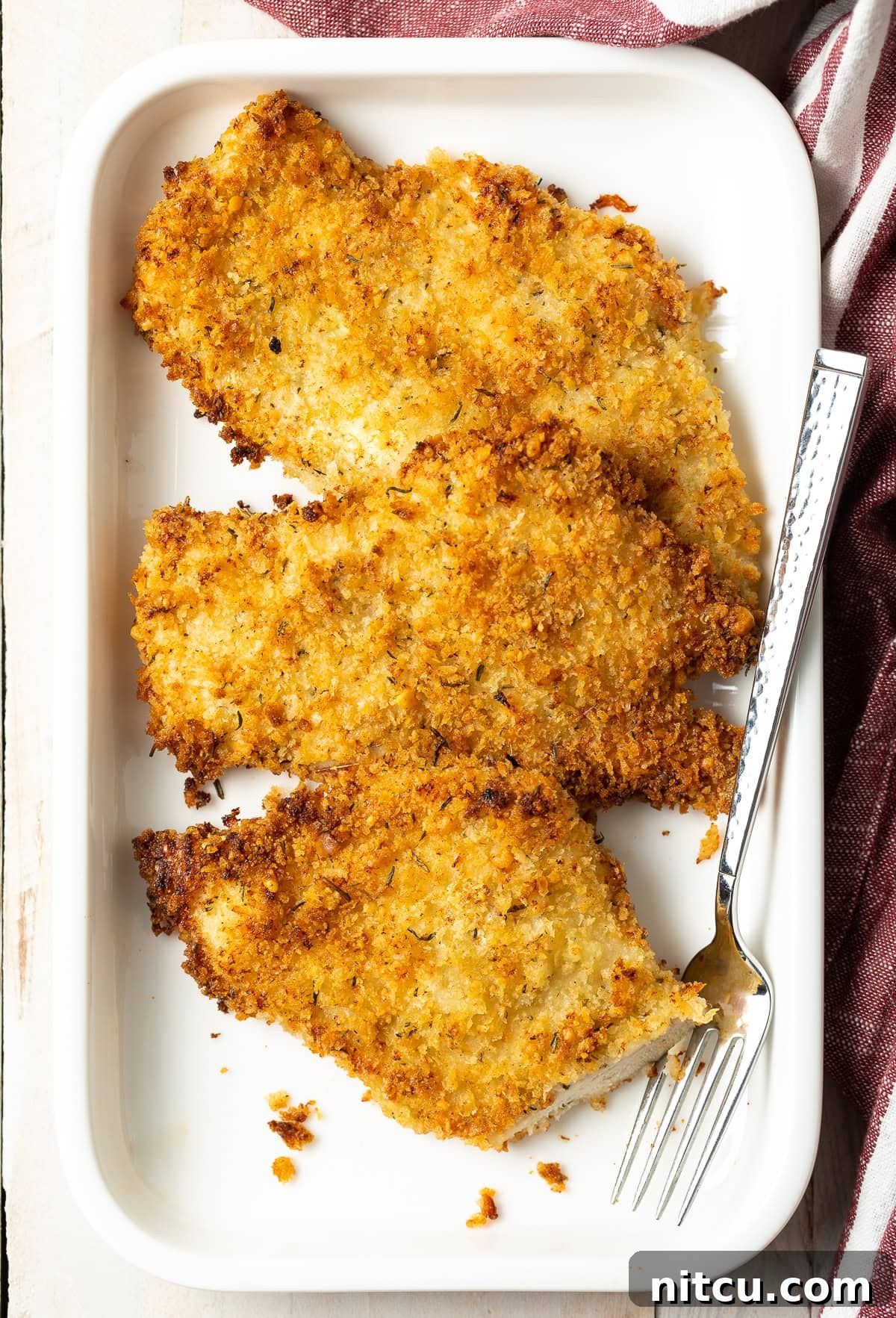 Golden Baked Chicken Cutlets 13 Overhead shot of oven fried chicken on a platter, garnished with fresh parsley and lemon wedges.