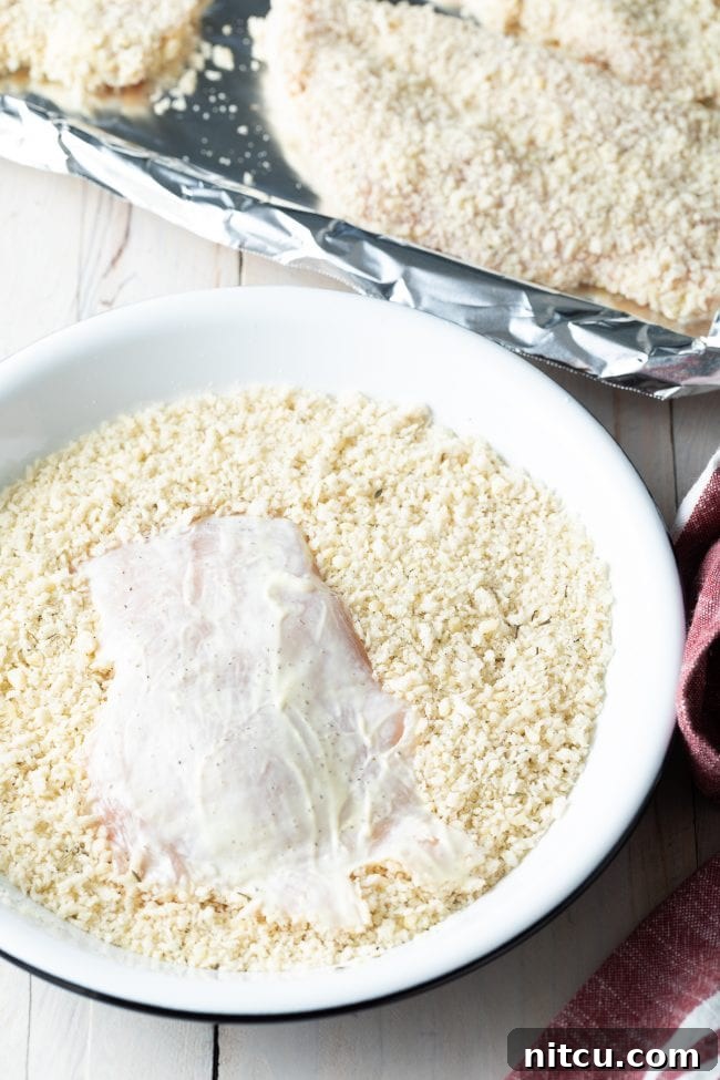 Golden Baked Chicken Cutlets 8 Mayo-coated chicken cutlet being carefully covered in the breadcrumb mixture, ensuring even coverage.
