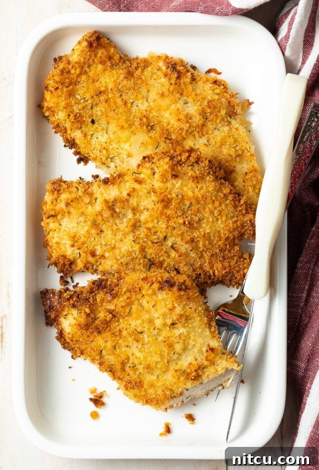 Golden Baked Chicken Cutlets 10 Plated cooked chicken cutlet with a fork and bite taken out, showing the juicy interior.