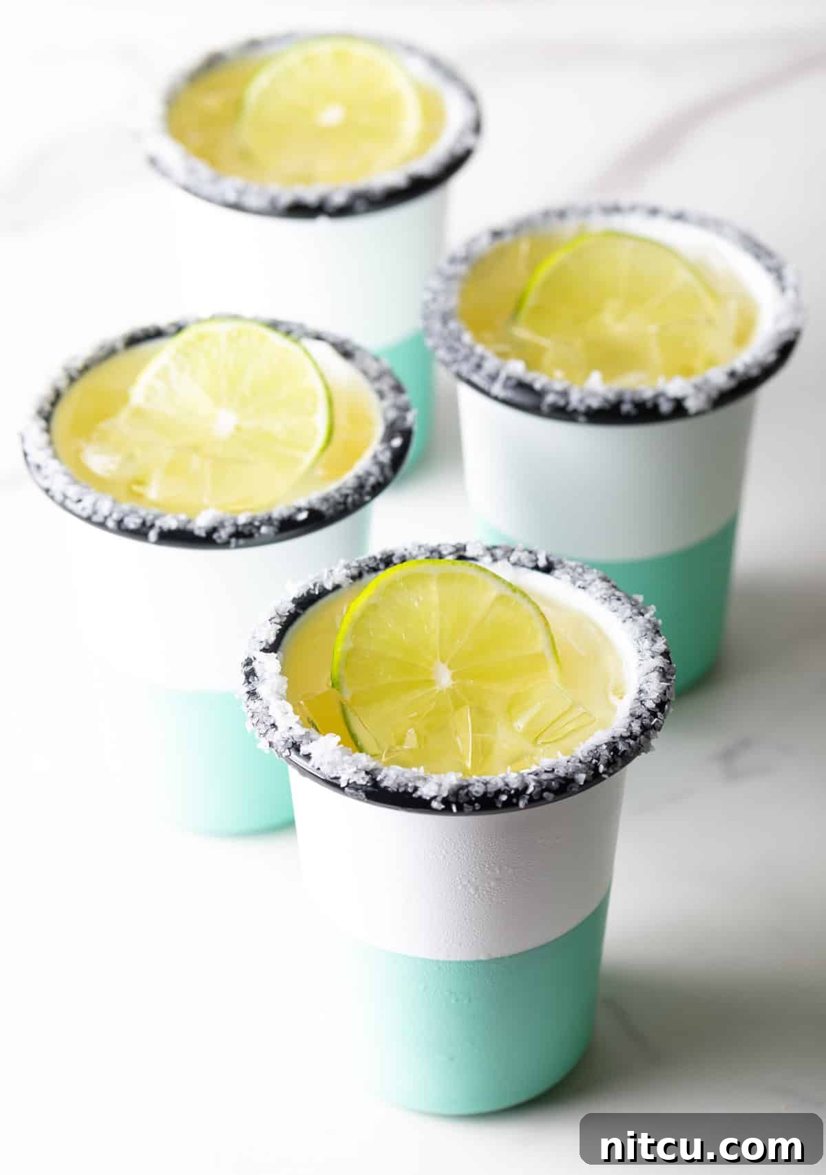 Zero-Proof Margarita 5 4 white and green-striped cups with margaritas on the rock, with salt around the rim and a slice of lime in the drink.