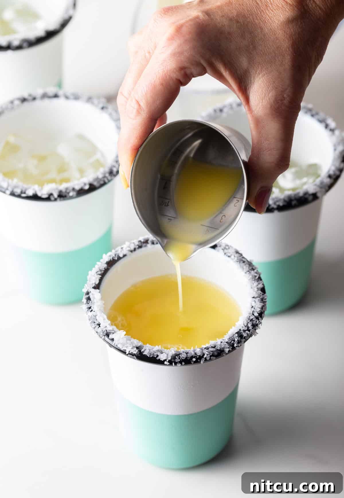 Zero-Proof Margarita 7 Hand pouring juice from a metal shot glass into a cup with a salted rim.