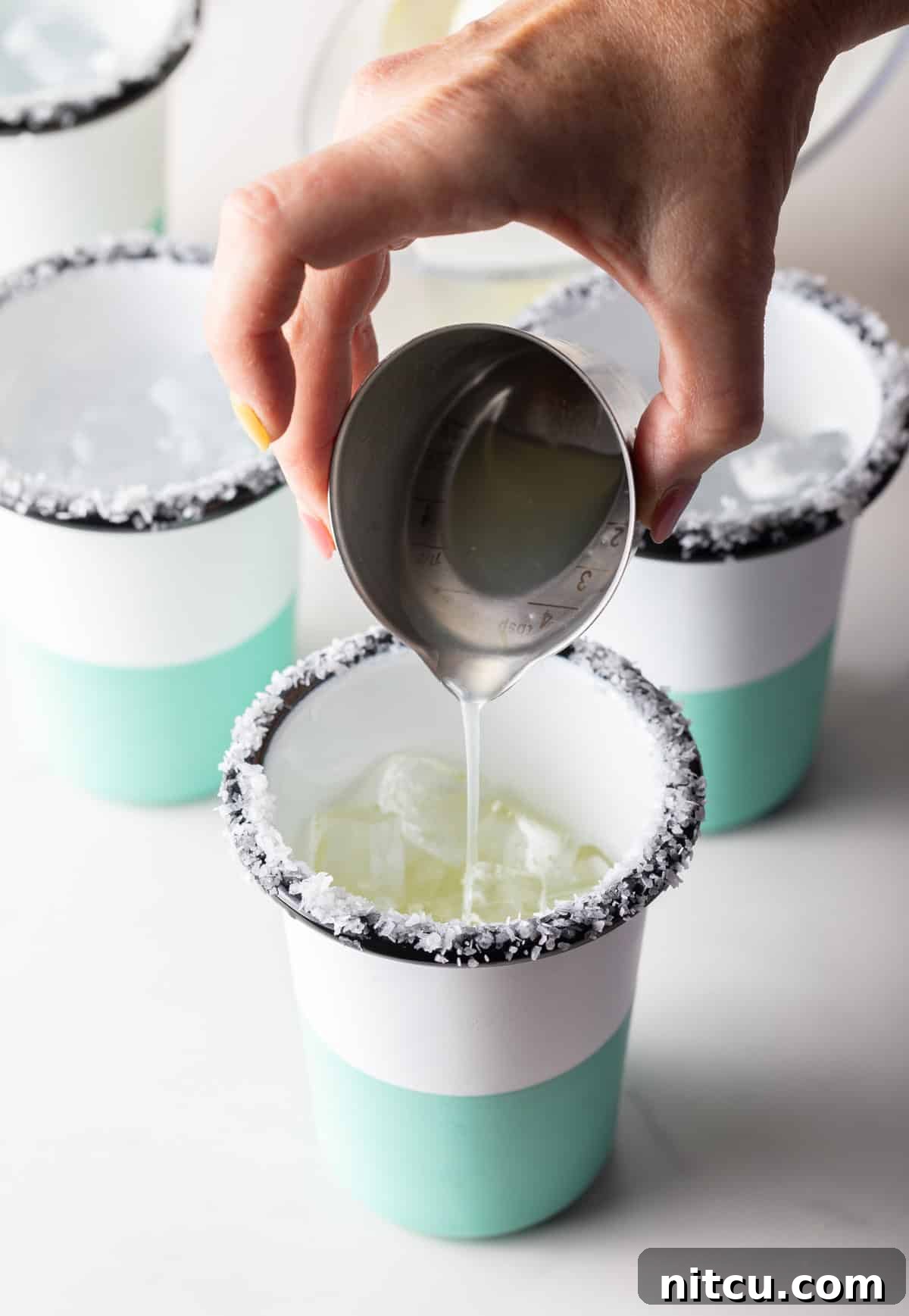 Zero-Proof Margarita 8 Hand pouring liquid from a metal shot glass into a cup with a salted rim.