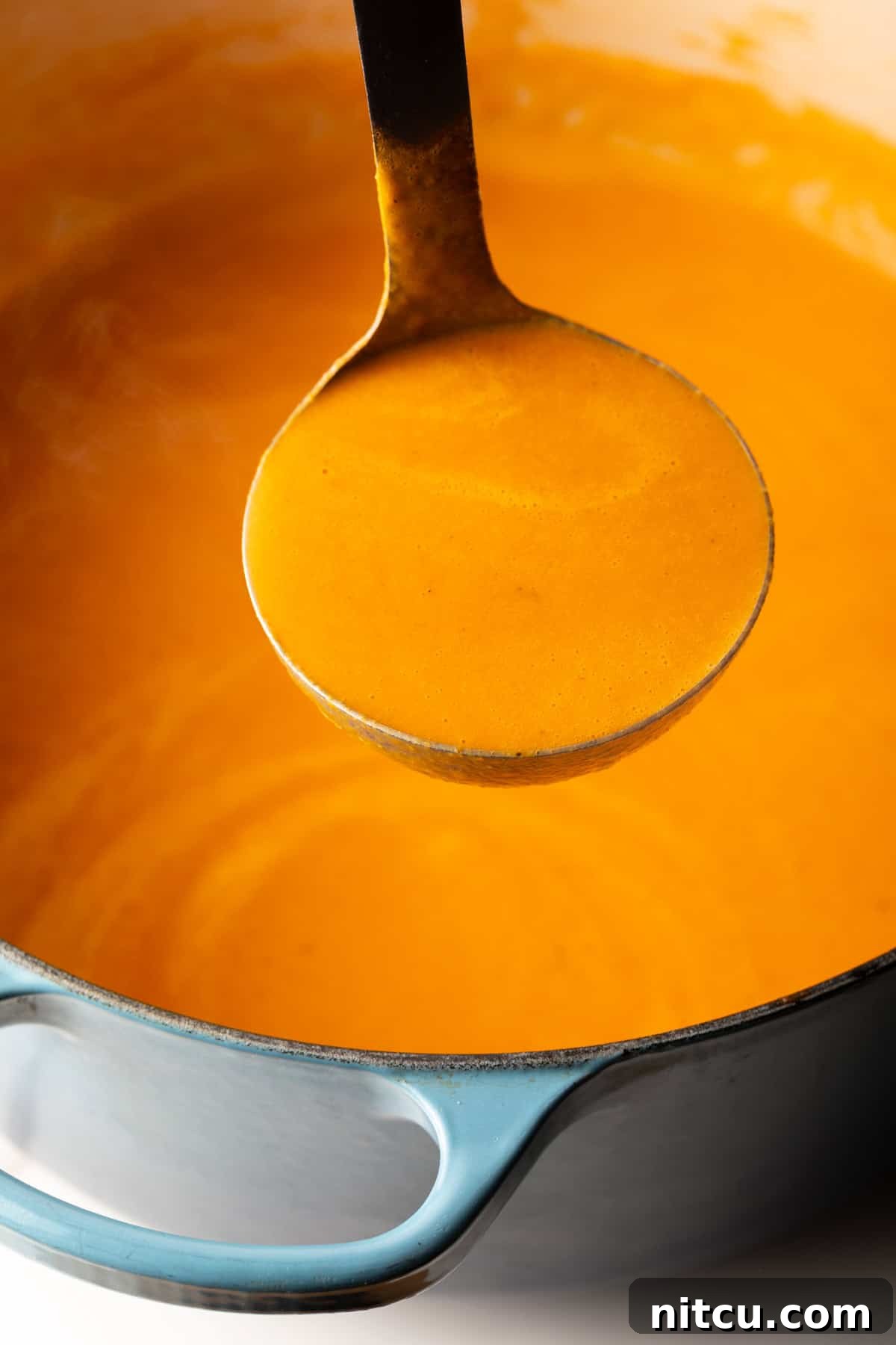 Smoky Red Pepper Bisque 12 A ladle filled with rich, creamy roasted red pepper Gouda soup, held up to the camera to showcase its smooth and inviting texture.