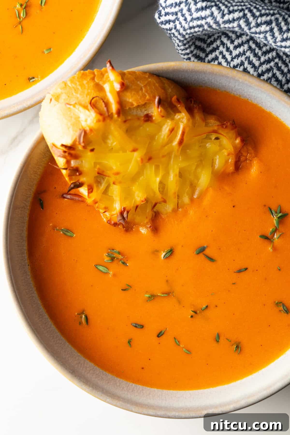 Smoky Red Pepper Bisque 13 A close-up of a bowl of creamy roasted red pepper Gouda soup, garnished with fresh herbs and a slice of golden-brown cheesy baguette toast, ready to be enjoyed.