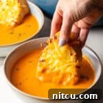 Smoky Red Pepper Bisque 15 A hand holding cheesy bread that is being dipped into a bowl of roasted red pepper soup.