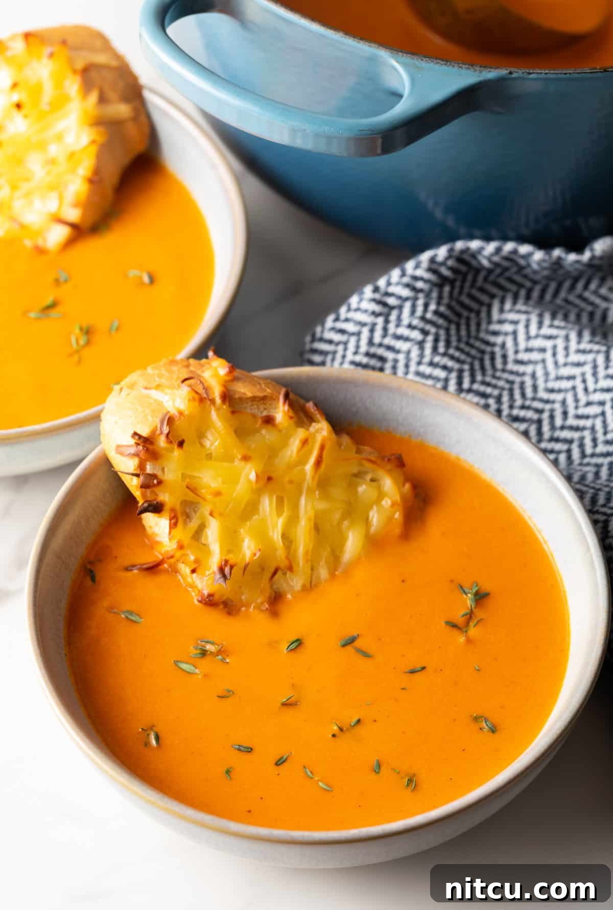 Smoky Red Pepper Bisque 3 A beautifully presented bowl of creamy roasted red pepper Gouda soup, garnished with fresh herbs and a slice of cheesy baguette toast resting on the rim.