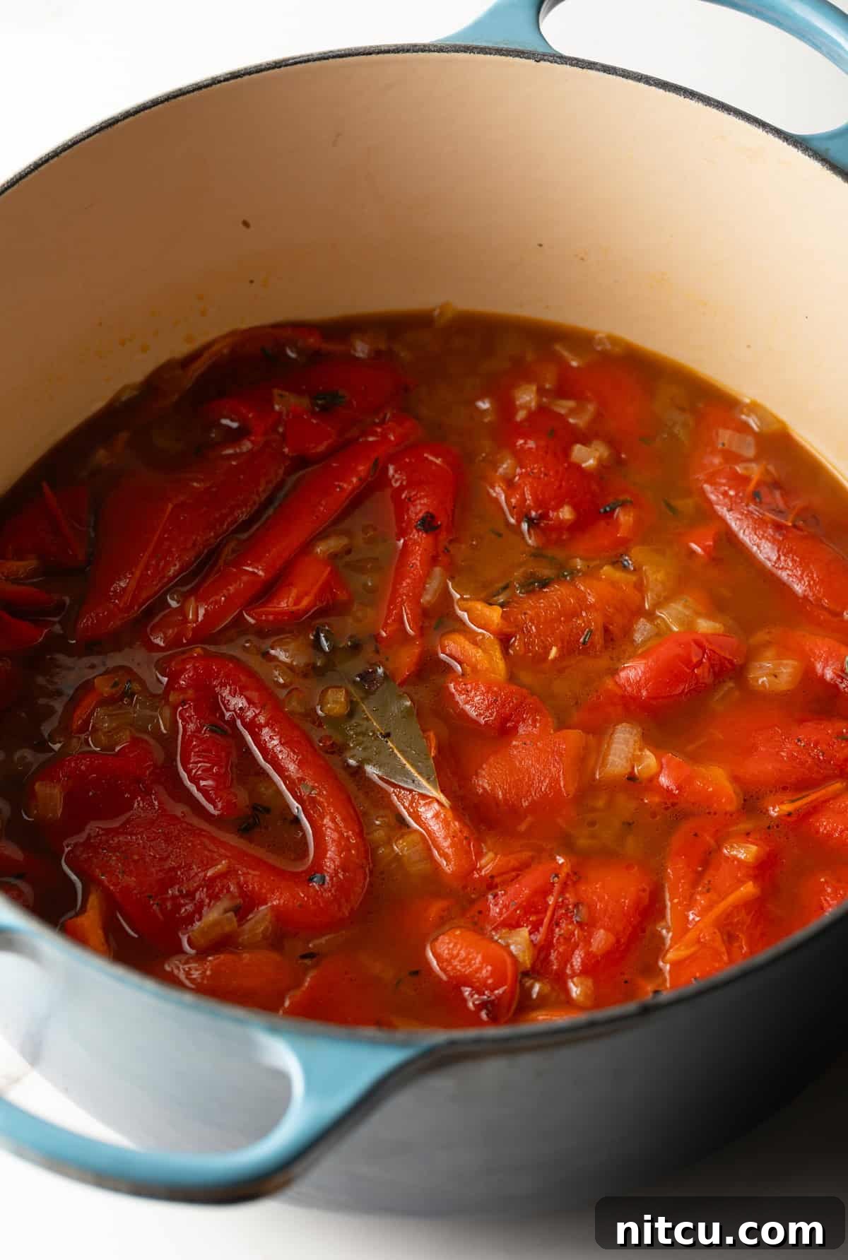 Smoky Red Pepper Bisque 9 Peeled, tender roasted red peppers submerged in a rich, simmering broth with herbs, ready to be blended into a creamy soup.