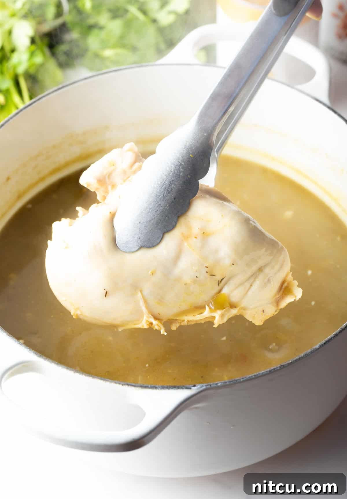 Tongs holding a cooked chicken breast over the pot.