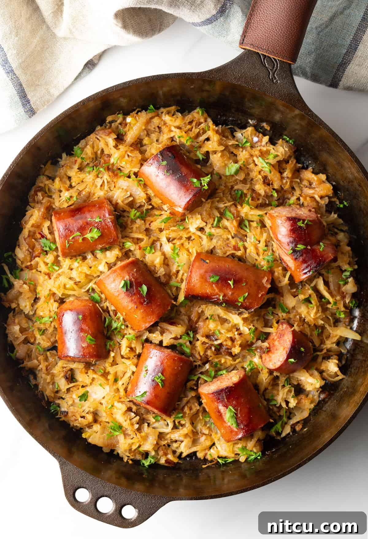 Top down view large skillet with browned sauerkraut and 8 pieces of cooked kielbasa sausage.