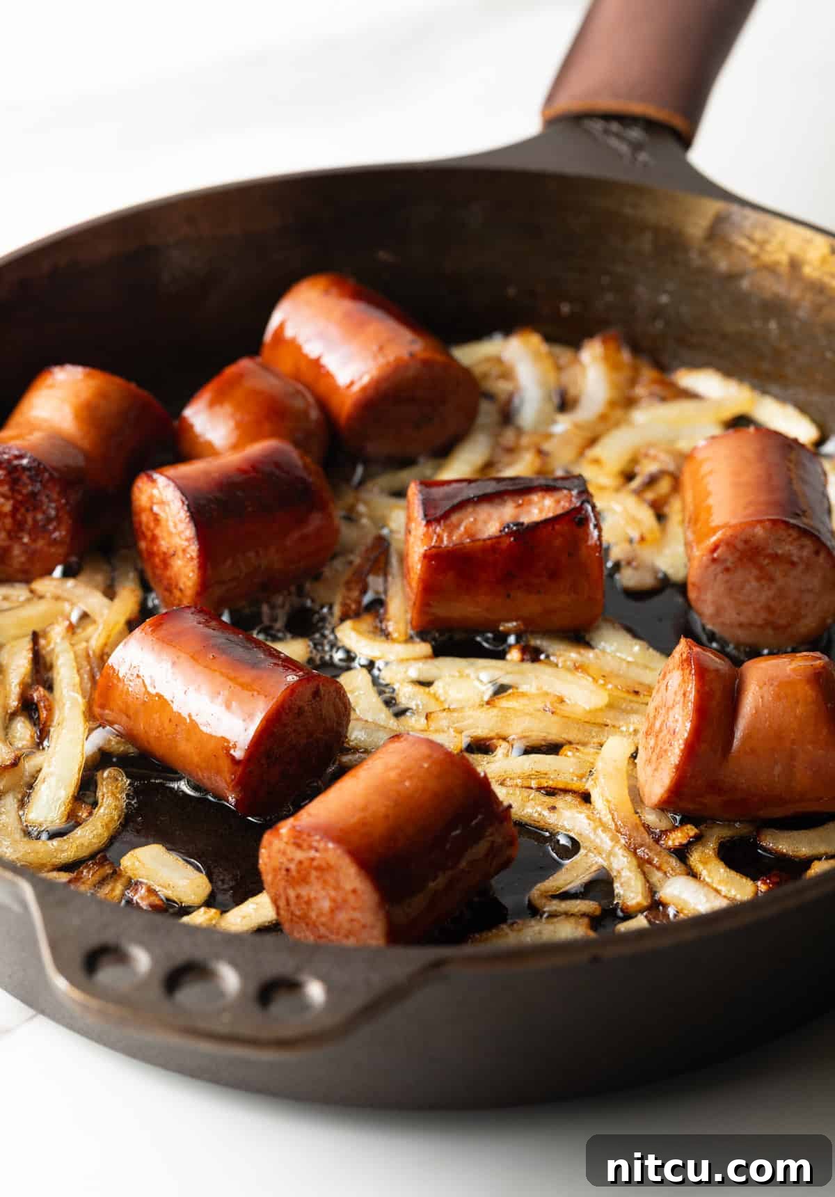 Seared pieces of sausage cooking in a cast iron skillet with onions.