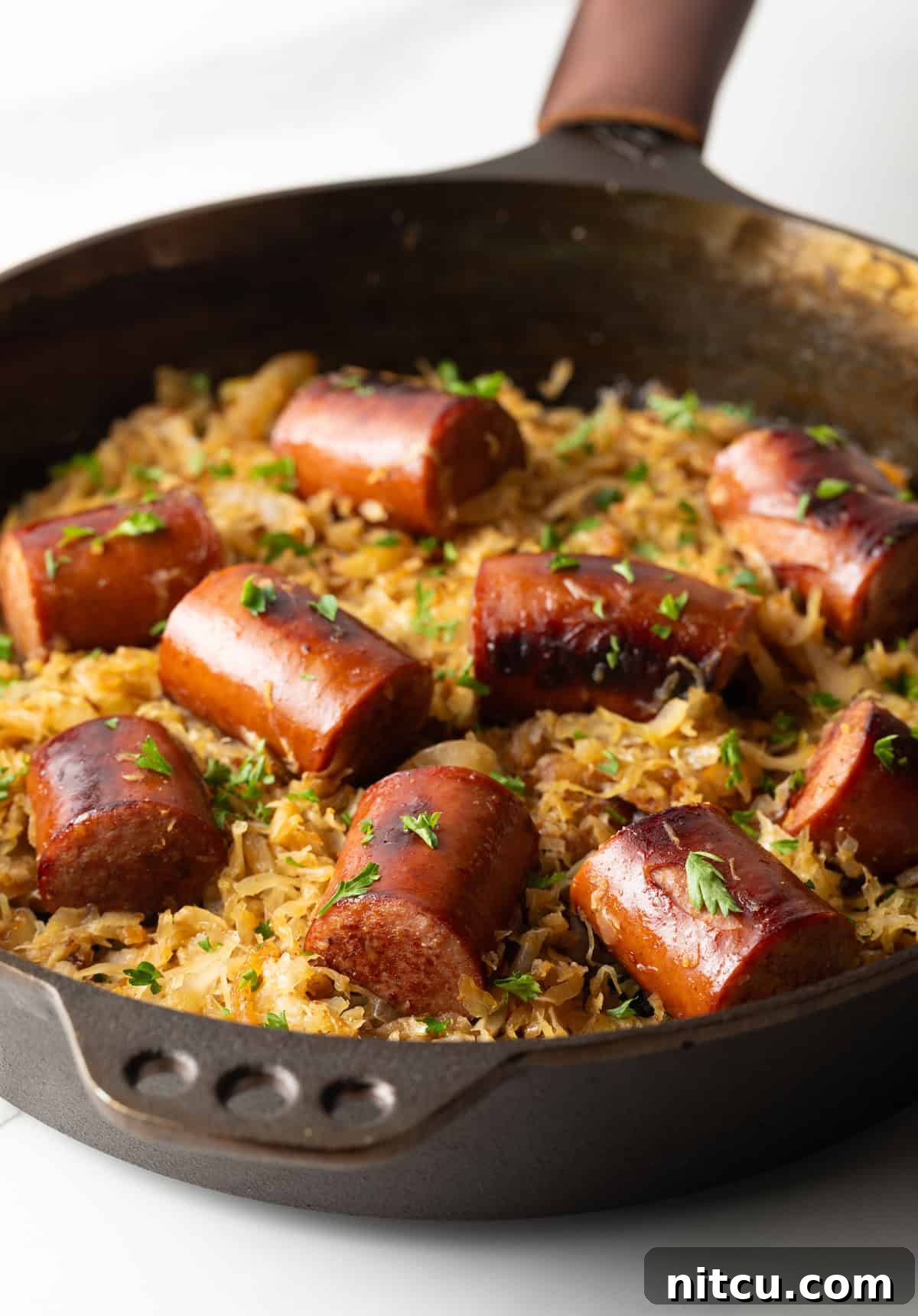Large skillet with kielbasa pieces on top of sauerkraut.